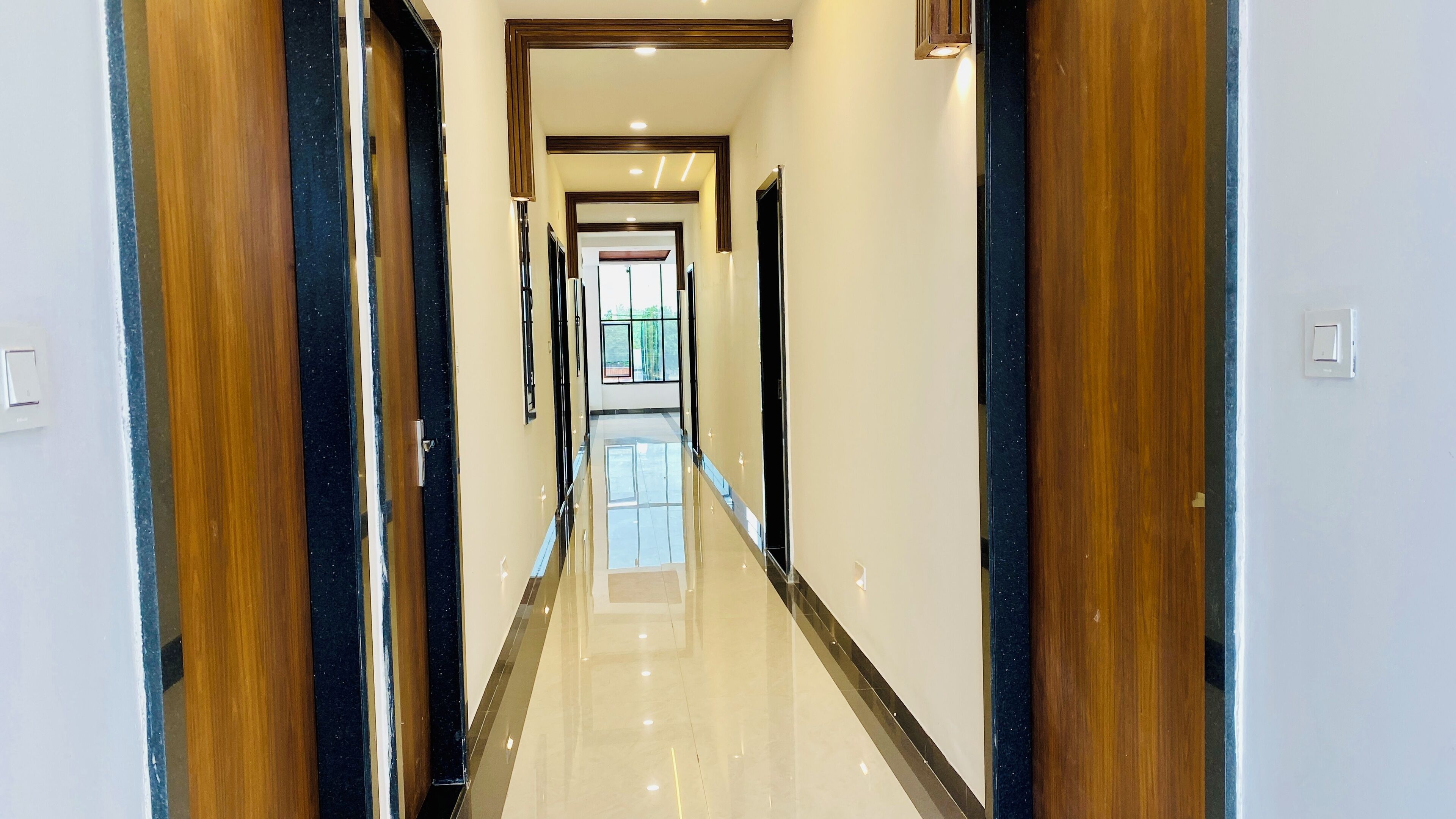 A long, polished hallway with wooden doors and a reflective floor, leading to a bright room with a large window.