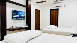 A hotel room with two beds, a TV mounted on the wall, a wooden desk, and a water bottle on the desk. - Hotel Shree Rameshwaram (Khandwa)