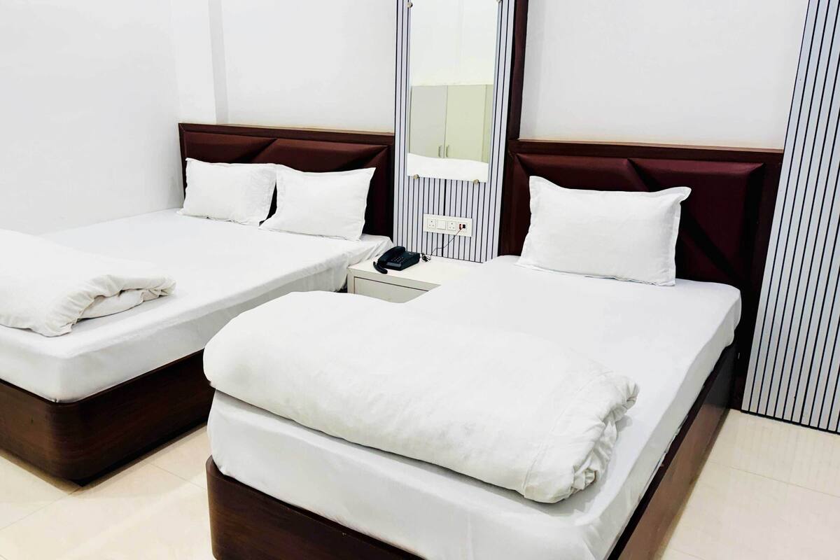 A hotel room with two single beds, a bedside table with a phone, and a mirror above the headboard.