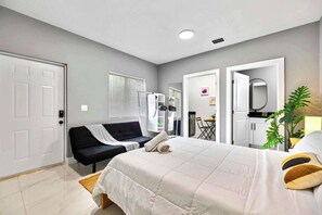 A modern hotel room with a bed, a sofa, a mirror, and a small table. - Spacious Miami Studio | Minutes to Wynwood (Miami)