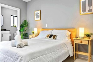 A neatly made bed with white bedding, a bedside table with a lamp, and a small plant on the nightstand. - Spacious Miami Studio | Minutes to Wynwood (Miami)