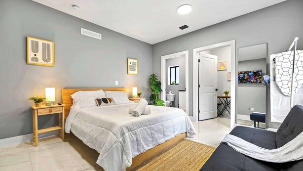A modern bedroom with a bed, bedside tables, a nightstand, a sofa, a mirror, and a door leading to another room. - Cozy Studio in Miami Near Wynwood Prime Location (Miami)