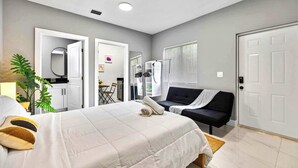 A hotel room with a bed, a sofa, a mirror, a plant, and a door. - Cozy Studio in Miami Near Wynwood Prime Location (Miami)