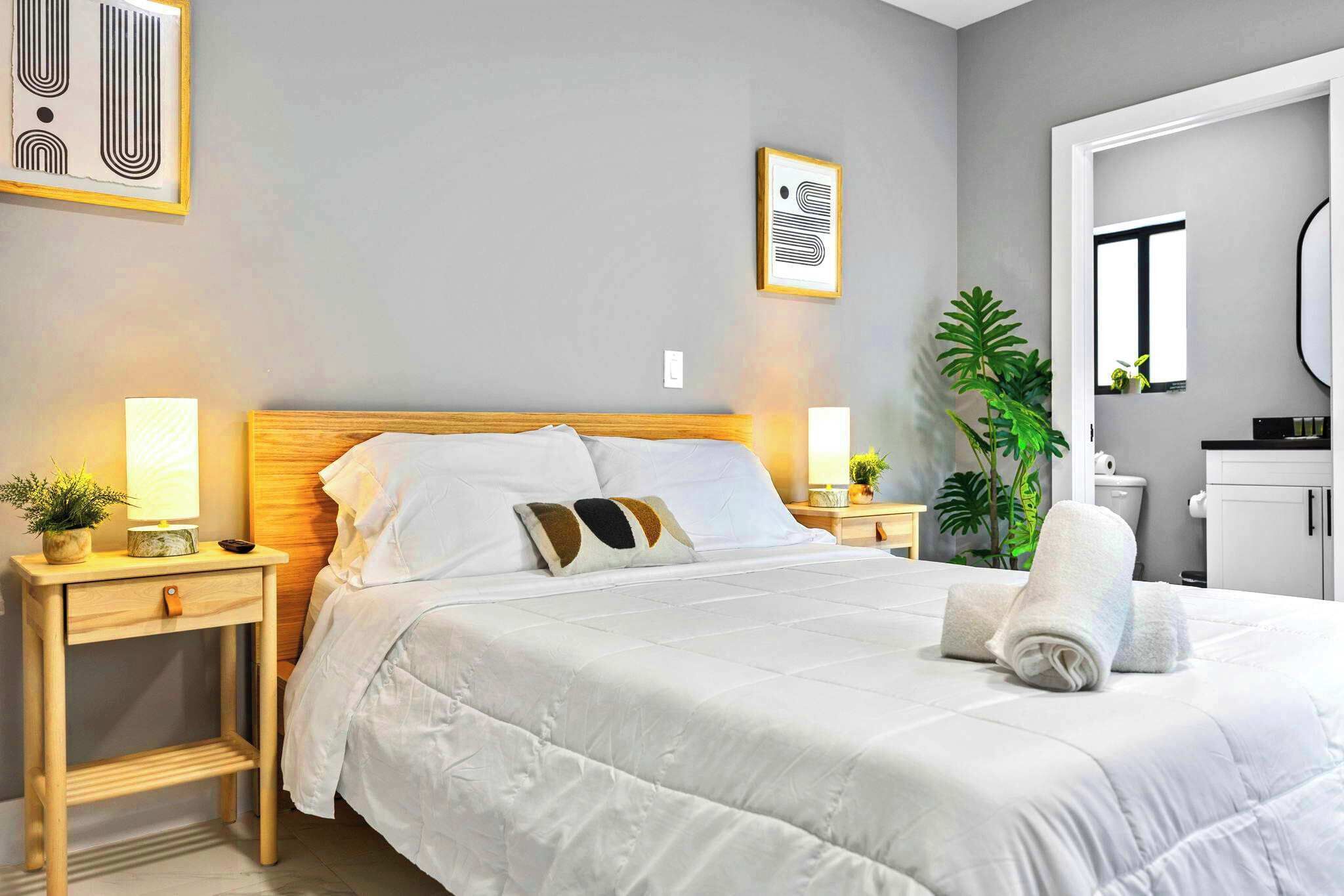 A neatly made bed with white linens, a wooden headboard, and a bedside table with a lamp and a small plant.