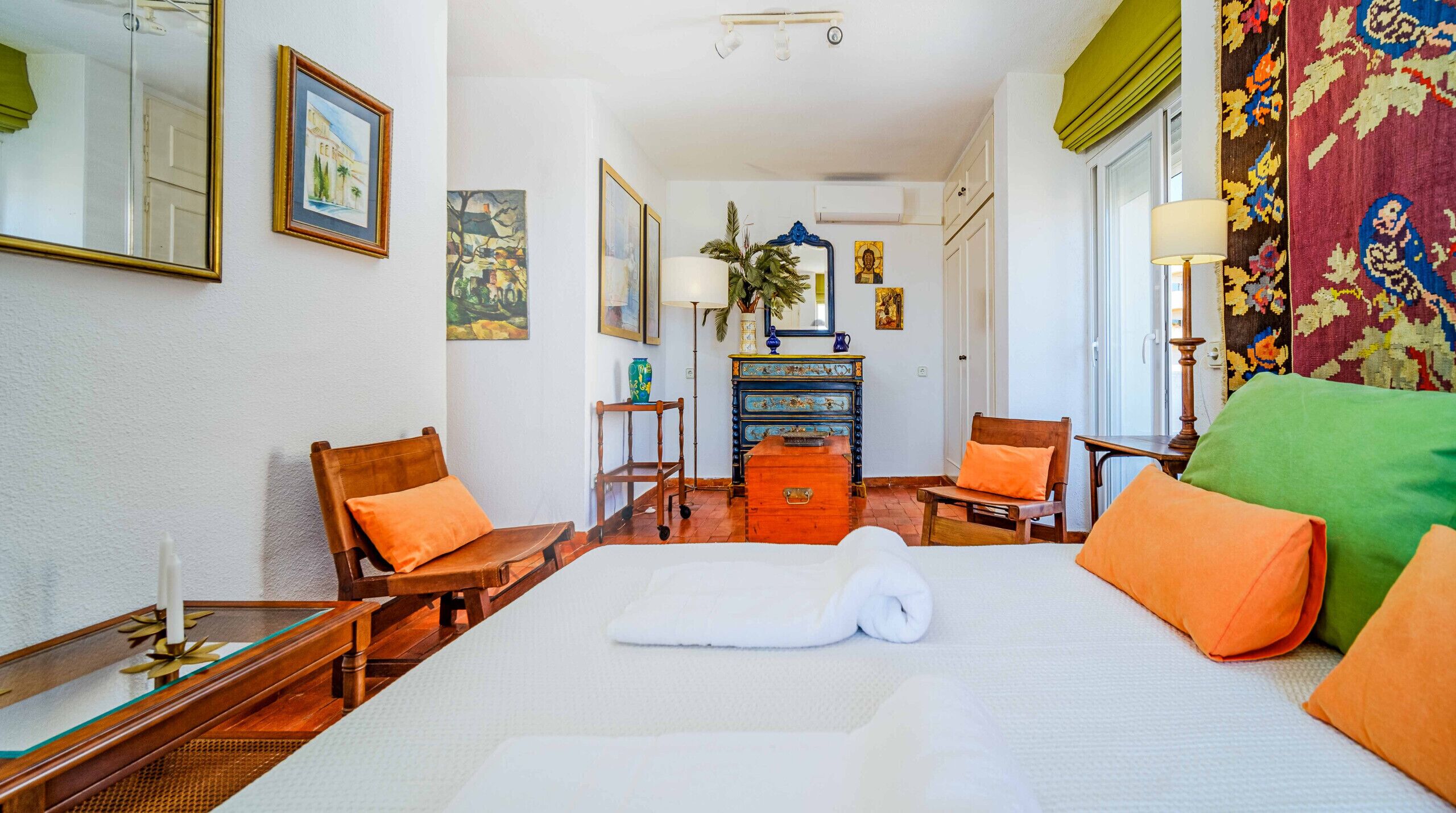 A hotel room with a large bed, two wooden chairs, a small table, a dresser, and a mirror.