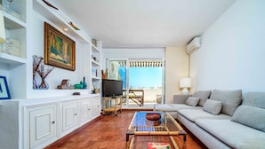 Una sala de estar con sofá, televisor, estantería y vistas al exterior.