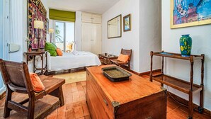 Una habitación con una cama, una mesa de madera, una silla, una mesita con velas y un cuadro en la pared.