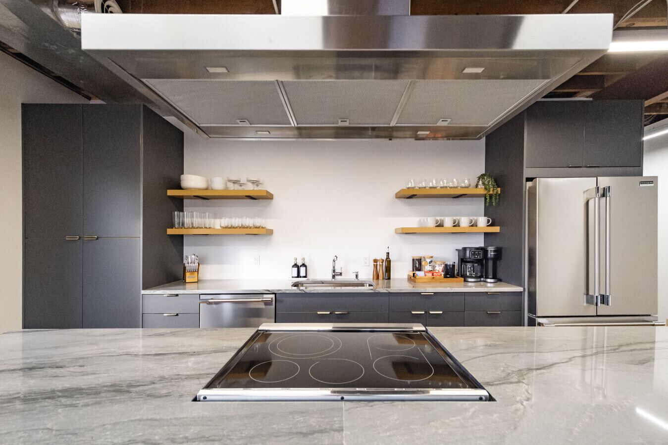 A modern kitchen with a central island, stainless steel appliances, and wooden shelves.