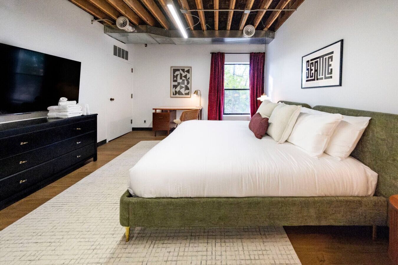 Une chambre moderne avec un grand lit, une télévision, un bureau et une fenêtre avec des rideaux.