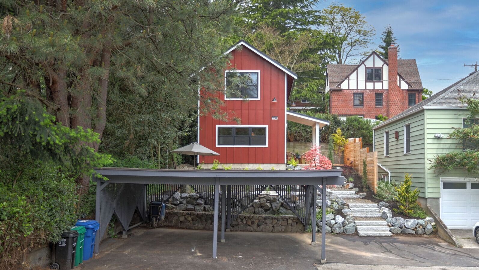 A red house with a covered patio, a stone wall, and a garage.
