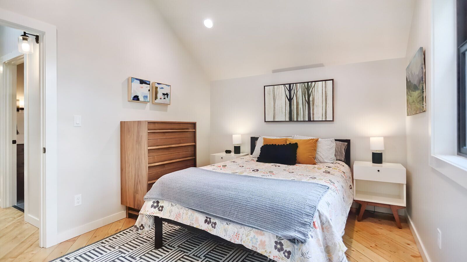A bedroom with a bed, bedside tables, a wardrobe, and artwork on the walls.