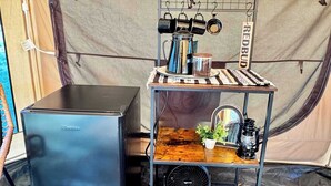 Una kitchenette compacta con refrigerador, cafetera y una pequeña repisa con una planta y un farol.