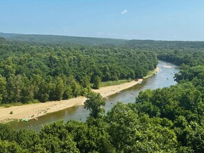 Une rivière bordée d’une forêt dense, avec des bateaux et des personnes sur l’eau.