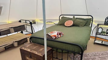 Een tent met een bed, een opbergkist en een klein tafeltje met een plant.