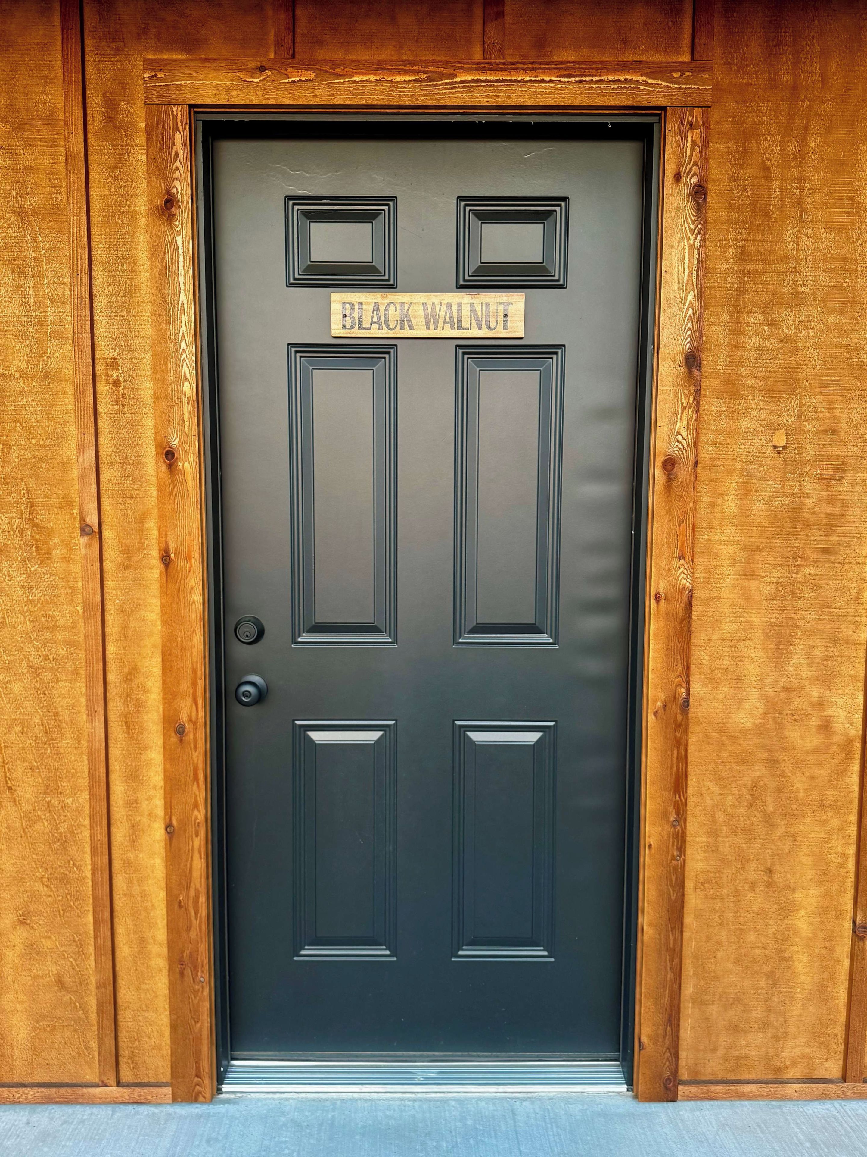 A black door with a sign reading "BLACK WALNUT" above it, framed by wooden panels.
