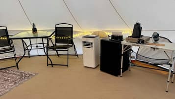 A tent interior with a table, chairs, a heater, and a portable gas stove.
