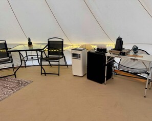 Interior de una carpa con una mesa, sillas, un calentador y una hornilla de gas portátil.