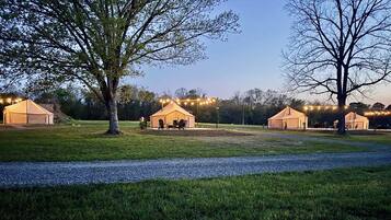 A campsite with three tents, each with a table and chairs, and string lights overhead.