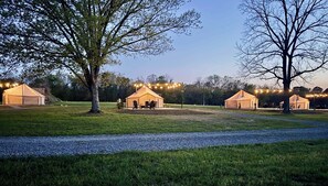 Ein Campingplatz mit drei Zelten, jeweils mit Tisch und Stühlen, und Lichterketten darüber.
