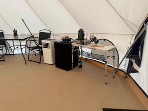 L'intérieur d'une tente, avec une table, des chaises, un chauffage portable, un ventilateur et une machine à café.