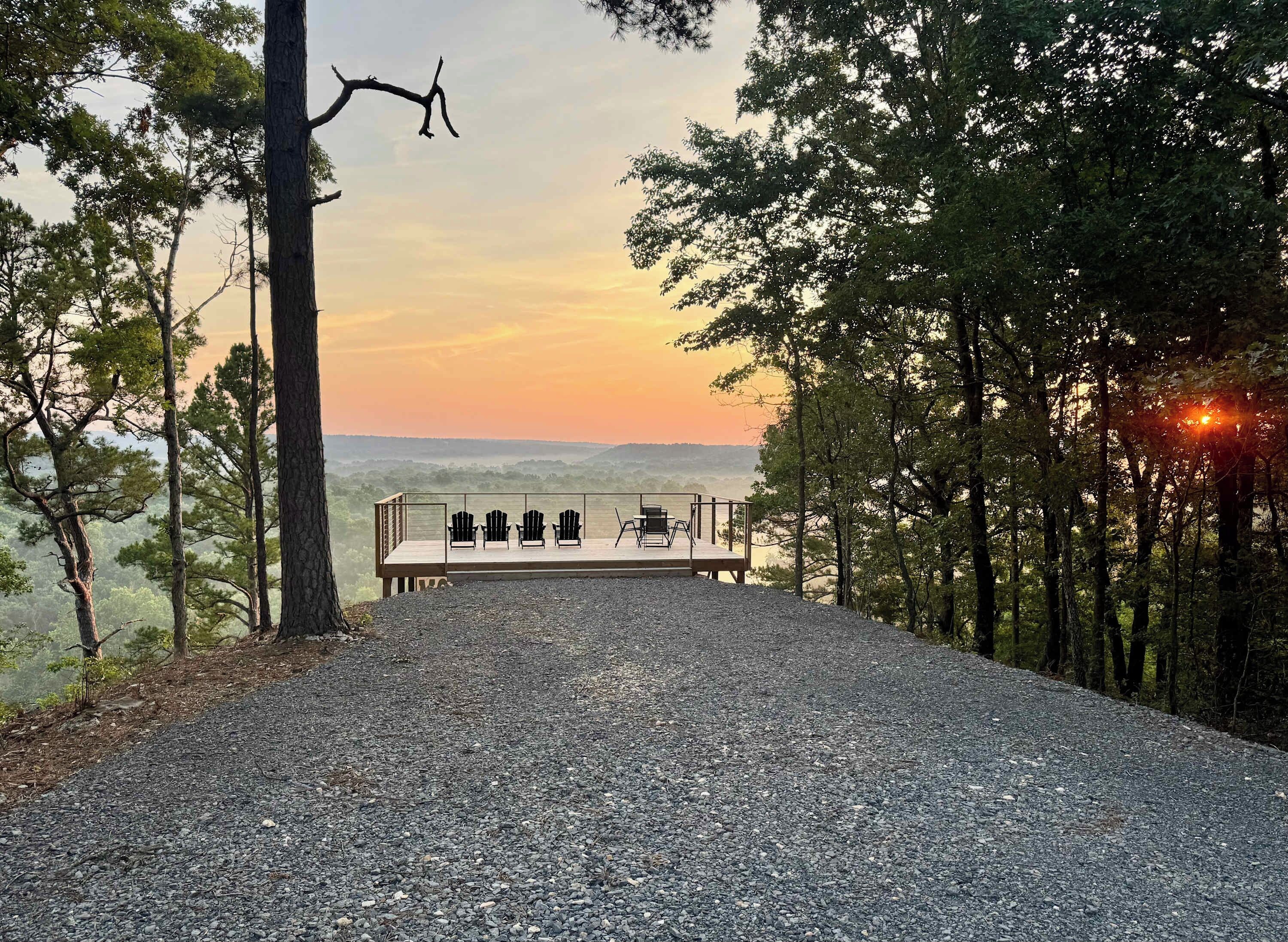 A gravel path leading to a wooden deck with outdoor seating, surrounded by trees and overlooking a landscape.
