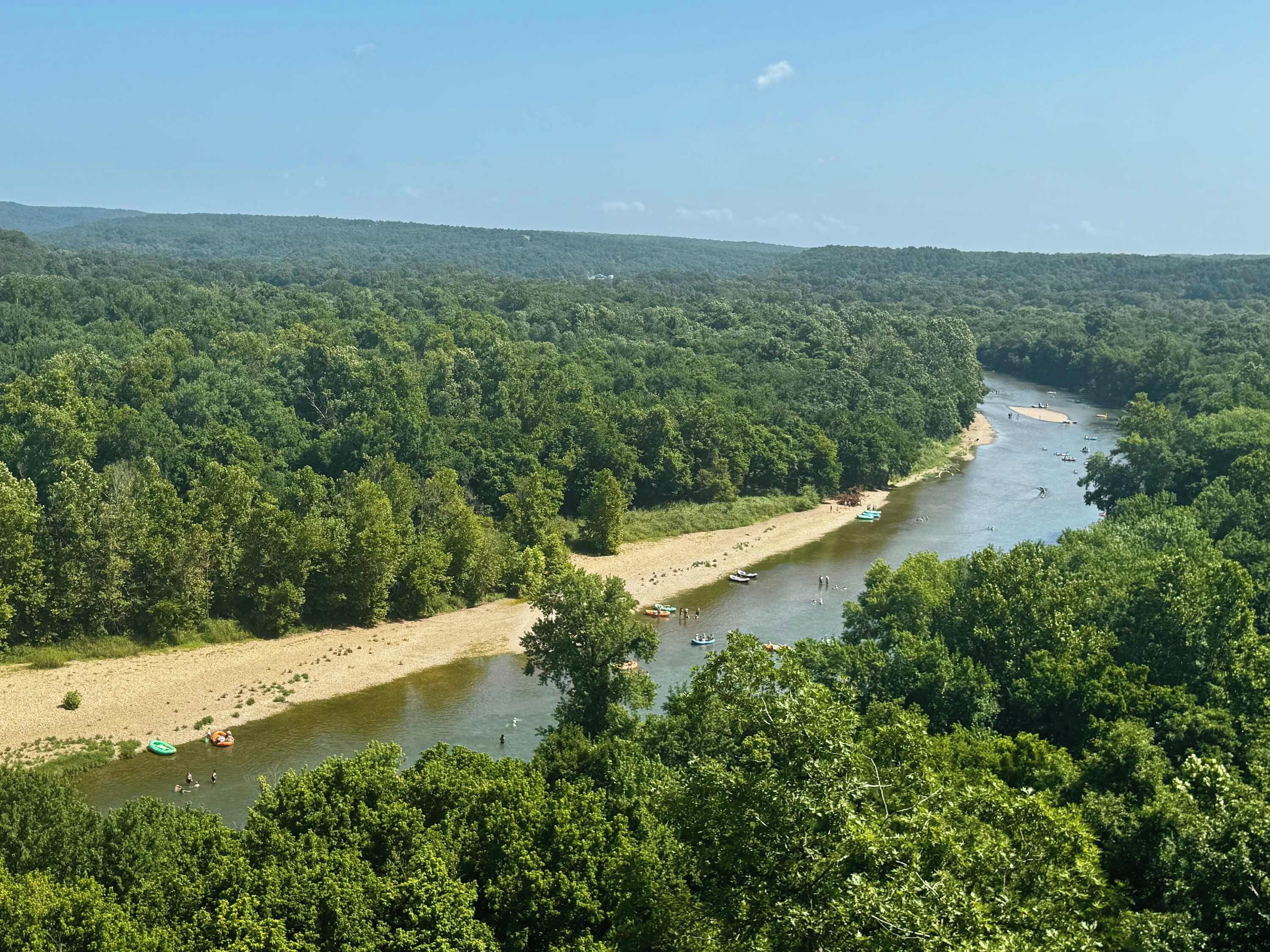 A river surrounded by dense forest with boats and people on the water.