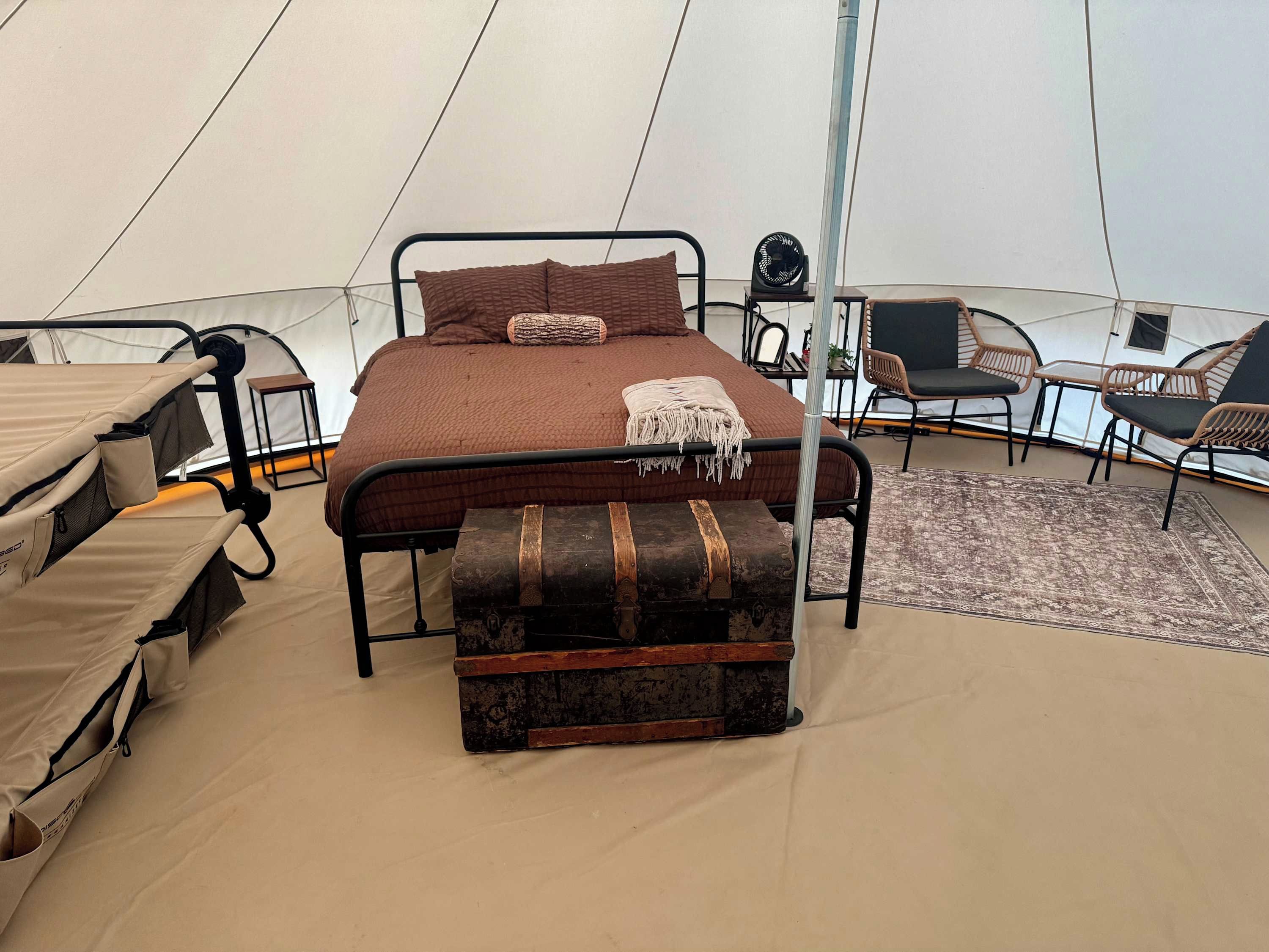 A tent with a bed, a bench, and seating areas.