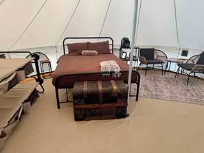 A tent with a bed, a bench, and seating areas.