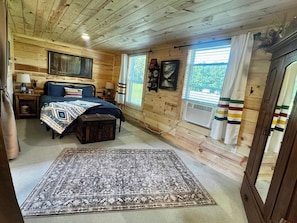 A wooden cabin bedroom with a bed, bedside tables, a rug, and a window with curtains.