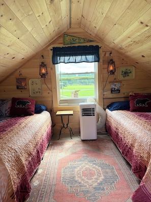A cozy attic bedroom with two beds, a window, a heater, and rustic decor.