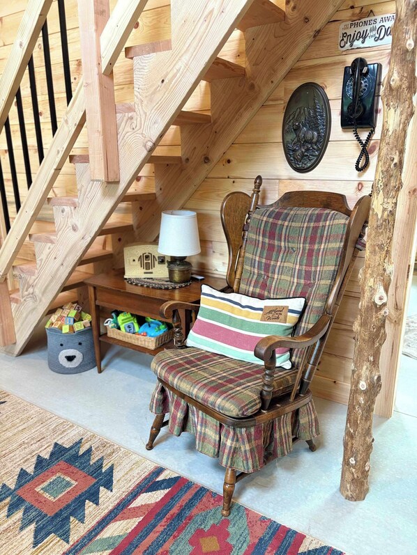 A wooden staircase, a wooden chair with plaid upholstery, a lamp, a basket, and a wall-mounted telephone.
