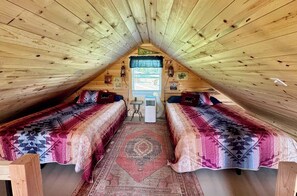 A cozy attic bedroom with two beds, a rug, and a small table.