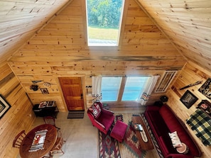 A cozy cabin interior with a wooden floor, a red sofa, a wooden table, and a window with curtains.