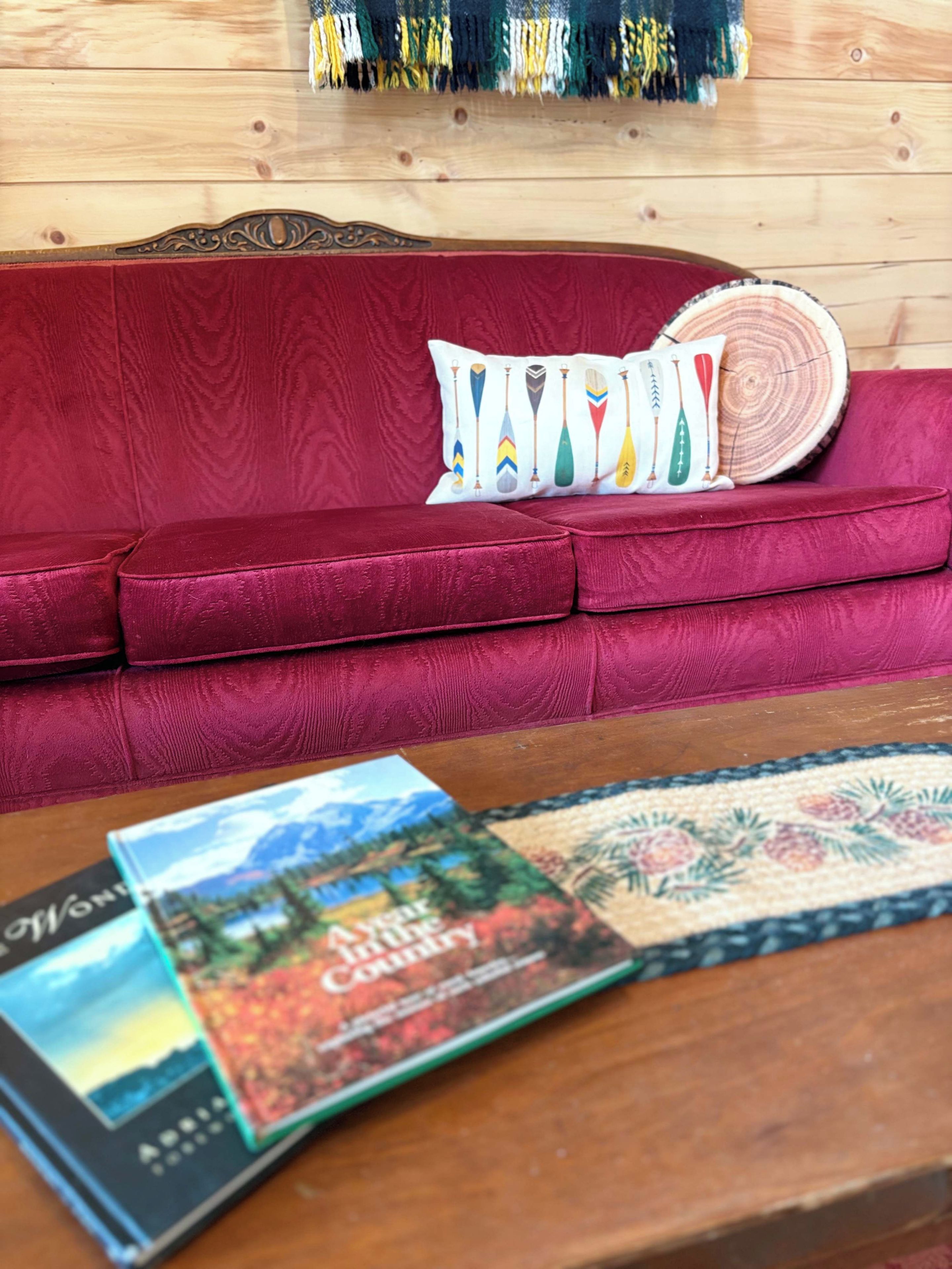 Ein rotes Sofa mit dekorativen Kissen, ein Holztischchen mit Zeitschriften und eine Holzwand mit einem Wandteppich.