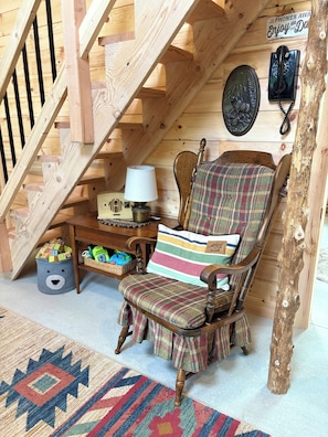 A wooden staircase, a wooden chair with plaid upholstery, a lamp, a basket, and a wall-mounted telephone.