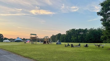 Eine grüne Wiese mit einem Spielplatz, Picknicktischen und Adirondack-Stühlen.