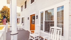 A white wooden house with a porch, rocking chairs, and a flag. - Downtown Ludlow, walk to ski shuttle, room for multiple families, pet friendly! (Ludlow)