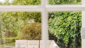 A view through a window of a garden with a sofa and a table. - Gorgeous House - Garden & Open Living (Cheltenham)