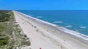 A beach with a long stretch of sand, a few umbrellas, and people walking along the shore.