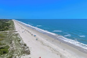 A beach with a long stretch of sand, a few umbrellas, and people walking along the shore. - High Tides, Good Vibes Resort Pool By Beach Star (Murrells Inlet)