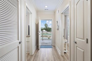 A hallway leading to a balcony with a view of a pool and trees.