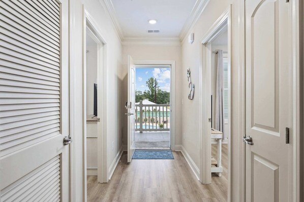 A hallway leading to a balcony with a view of a pool and trees.