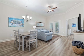 A dining area with a wooden table and chairs, a blue sofa, a ceiling fan, and a painting of a crab. - High Tides, Good Vibes Resort Pool By Beach Star (Murrells Inlet)