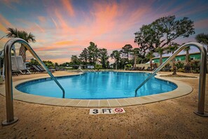 A swimming pool with a 3 FT no diving sign, surrounded by lounge chairs and palm trees.