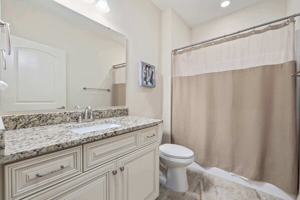 A bathroom with a sink, mirror, toilet, and shower curtain.