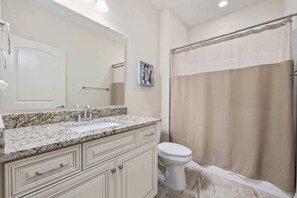A bathroom with a sink, mirror, toilet, and shower curtain.