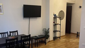Una sala moderna con comedor, piso de madera, un televisor de pantalla plana montado en la pared, un espejo redondo y un sofá azul.