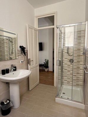 Un baño moderno con cabina de ducha de vidrio, un lavamanos pedestal y un espejo sobre él.