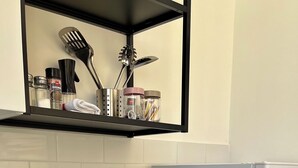 Una cocina con microondas, un horno Samsung, una encimera con dos copas de vino y una estantería con utensilios y recipientes de cocina.