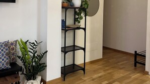 Una sala moderna con piso de madera, una estantería de metal negro con plantas, un sofá estampado y un televisor montado en la pared.